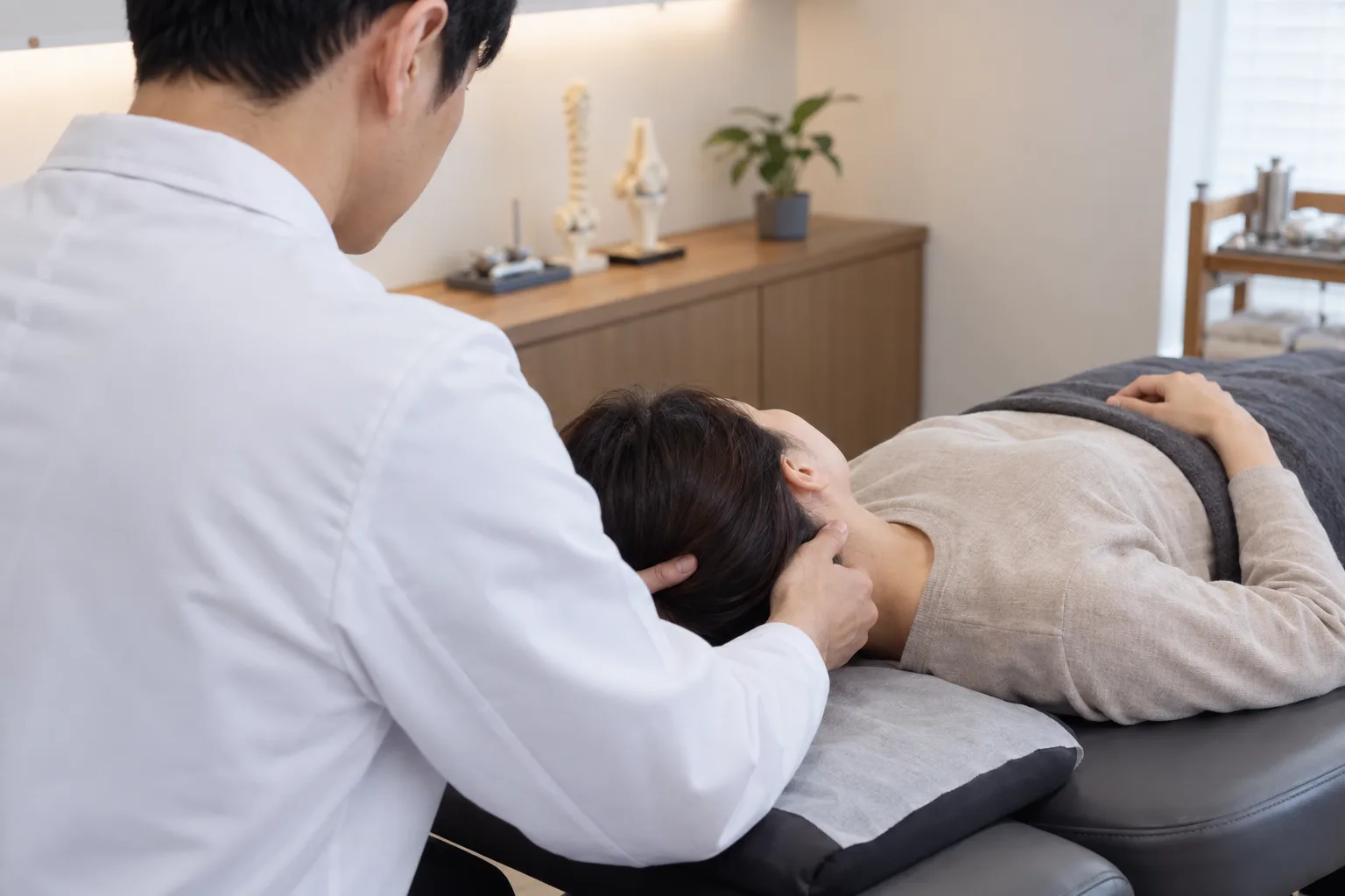 남성 한의사가 누운 환자의 목을 지지하며 부드럽게 경추를 살피는 장면